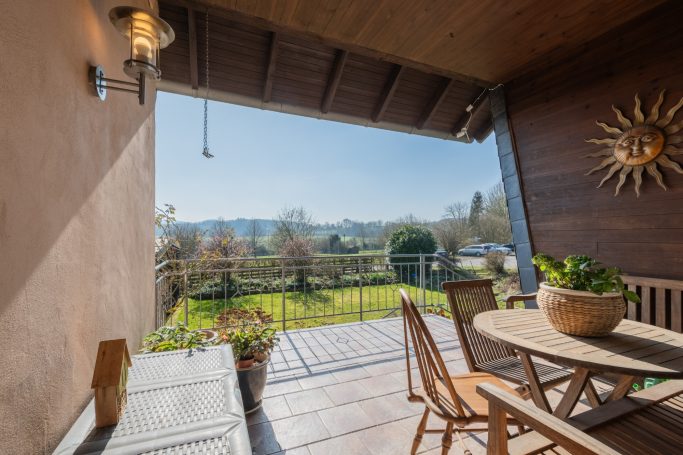 Ein sonniger Balkon mit Tisch, Stühlen und Blick auf eine grüne Landschaft.