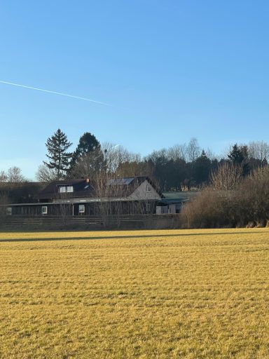 Unser Hof im Grünen mit blauem Himmel und Wiese im Vordergrund.