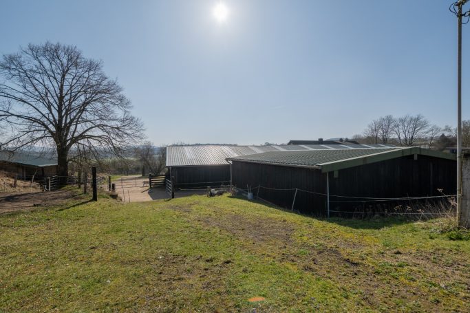 Landschaft mit einem Bauernhof, grünen Wiesen und klarem Himmel.