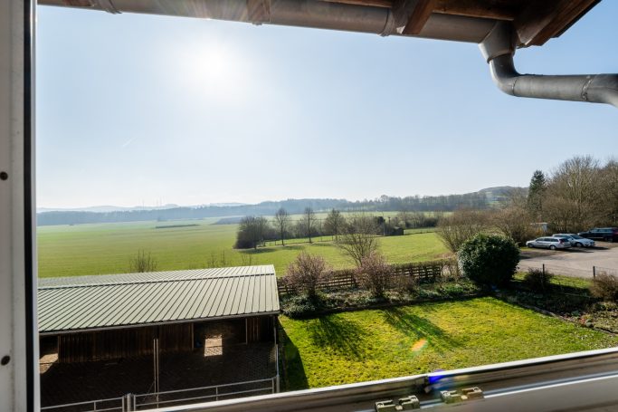Blick auf eine weite Landschaft mit Feldern und Bäumen an einem sonnigen Tag.